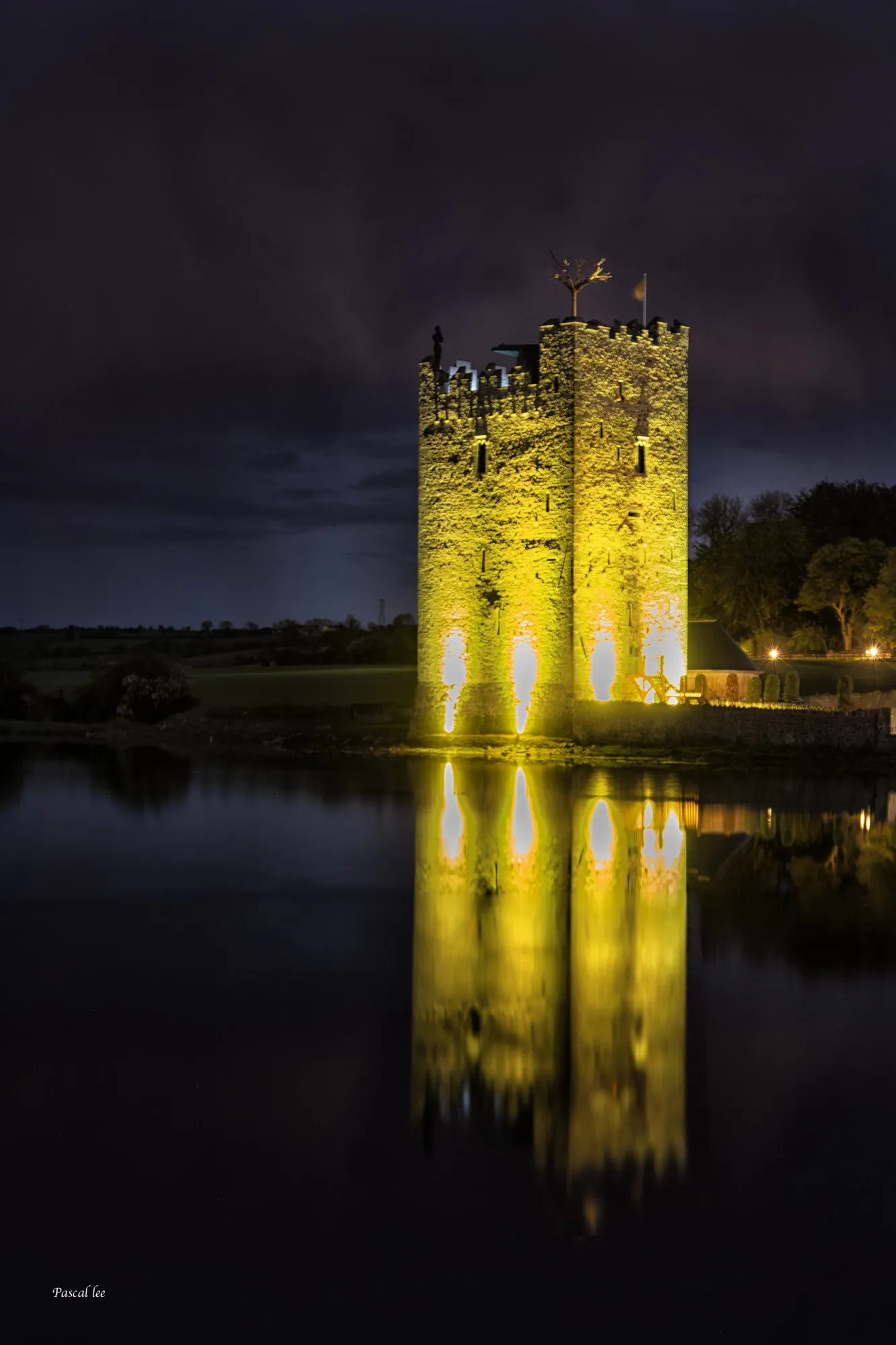 Belvelly Castle floodlit gold at night and reflected in still water