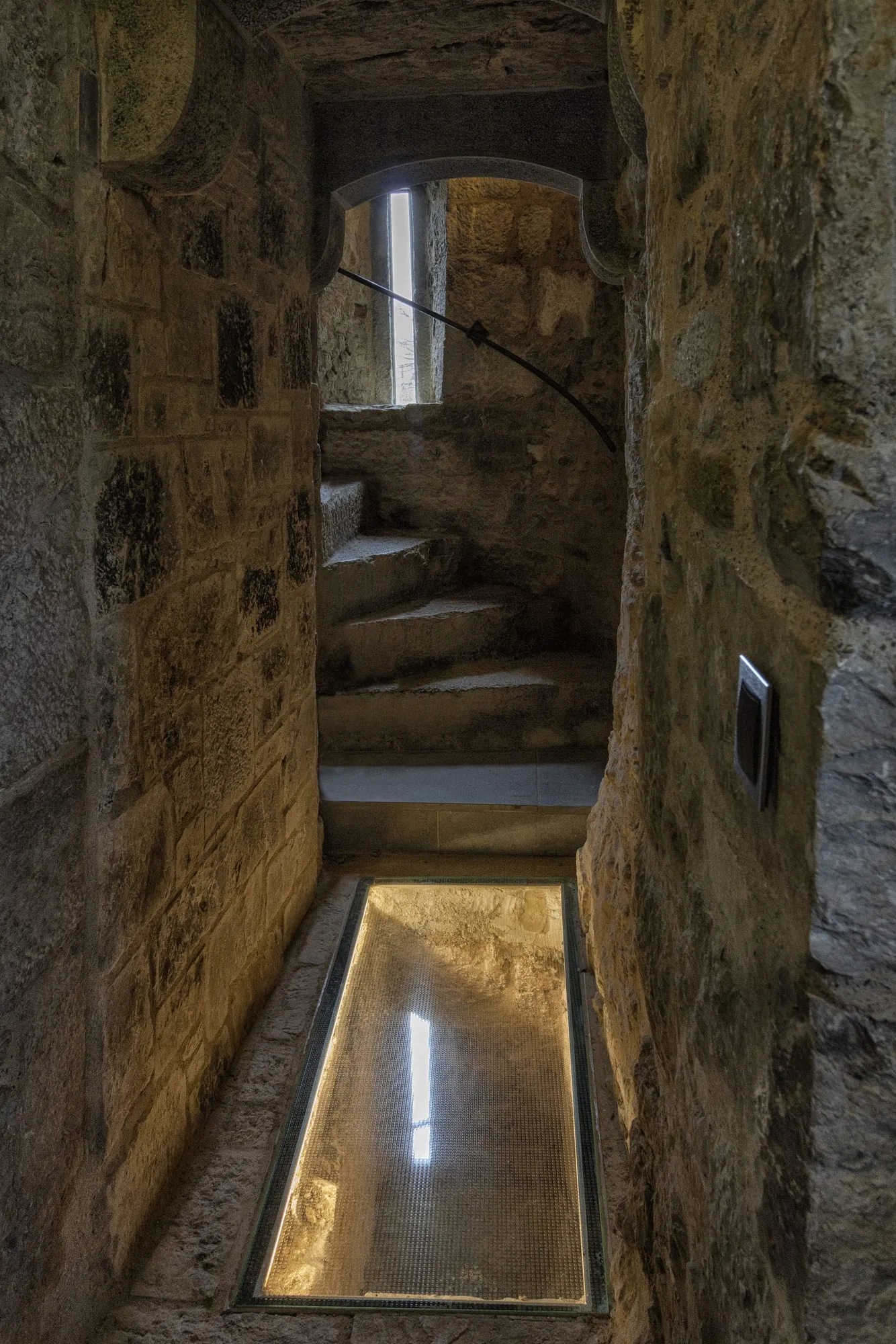 Narrow stone passage with a lit glass floor panel